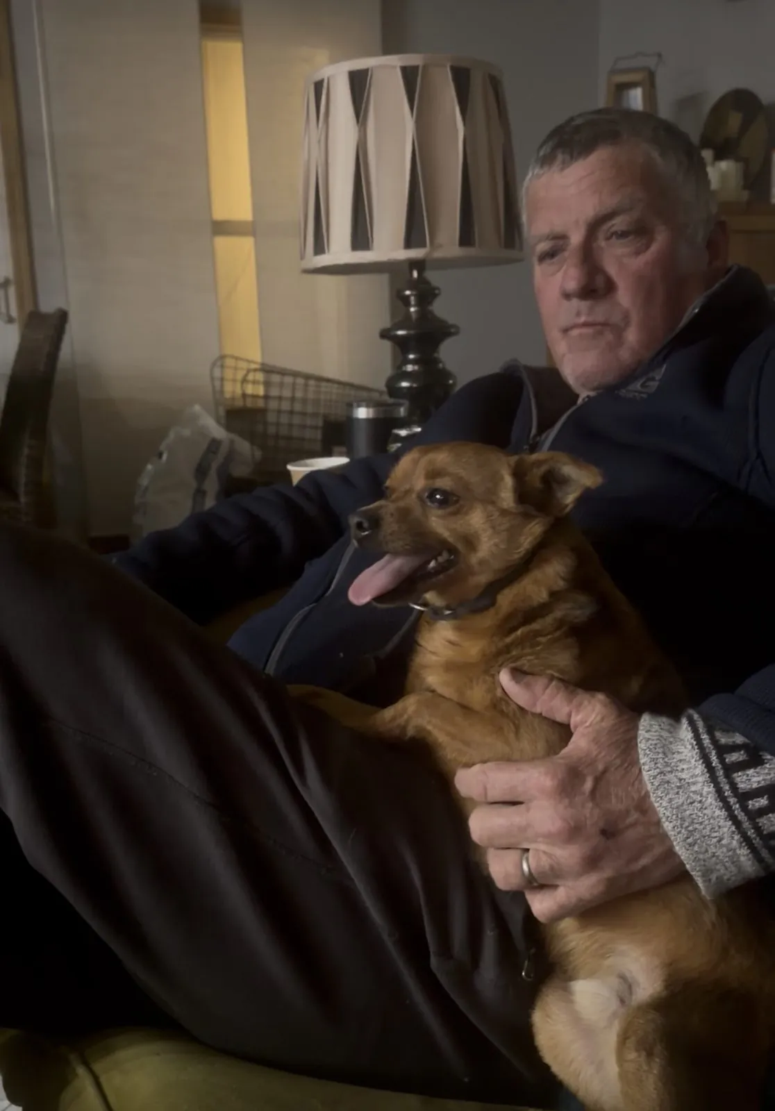 Joel Monroe relaxes in a living room chair with Bandit, a small tan dog, resting on his lap