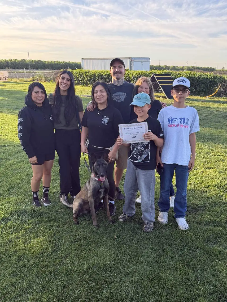 Family of seven smiling on a training field with their Belgian Malinois puppy and a Basic Obedience certificate