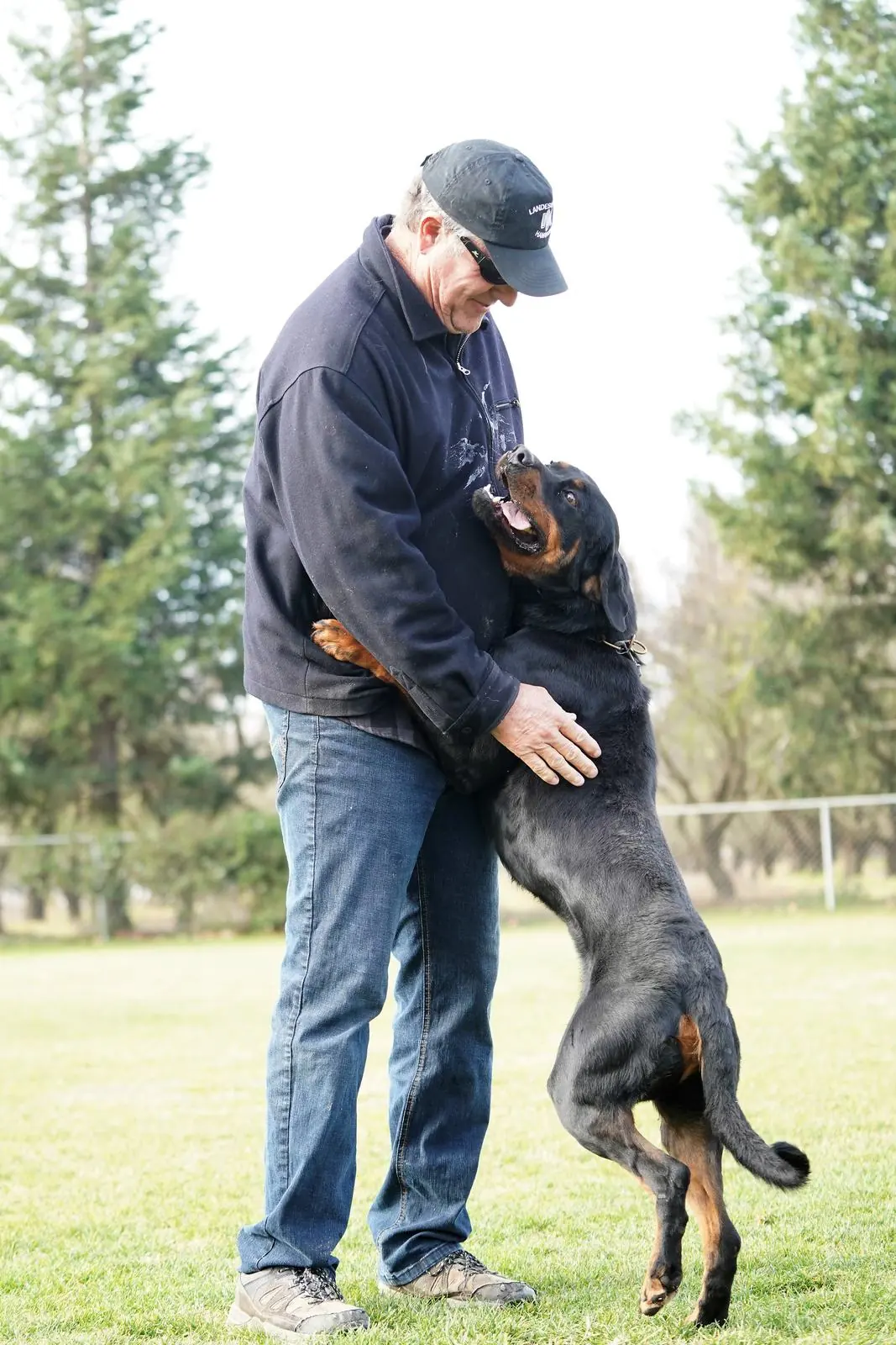 Joel Monroe smiles down at a Rottweiler who stands on its hind legs to greet him on a grassy training field